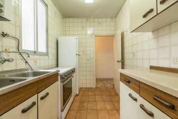 Old kitchen with old furniture in poor condition, white fridge, vintage tiles and aluminum window with translucent glass