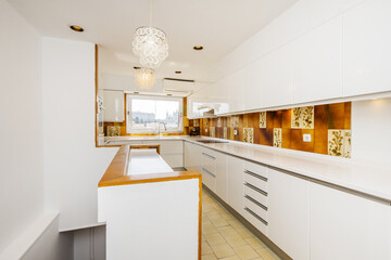 elongated kitchen with plain white cabinets, white faux stone countertops, outdated tiles and a window with a view in the background