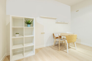 Living room corner with white wooden shelving, shelves on the wall and a wooden folding table with a white frame and matching chairs
