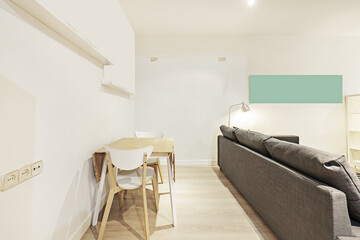 Living room corner with large gray fabric sofa and wooden folding table with white frame and matching chairs