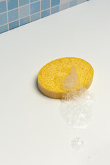 A yellow synthetic bath sponge with soap foam on a white surface