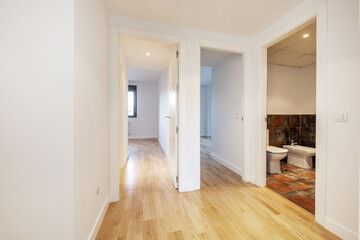 Distributor space of a house with wooden floors and white wooden access doors to a bathroom and empty rooms