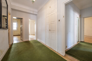 Distributor space of a house with wooden floors covered with green carpets, a built-in wardrobe and wooden access doors to empty rooms
