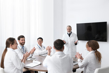 Fototapeta premium Team of doctors listening to senior speaker report near tv screen in meeting room. Medical conference