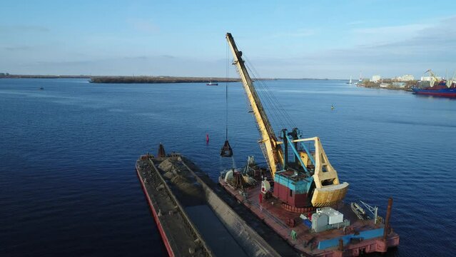 Aerial view. A dredging machine takes sand from the bottom of the river and loads it onto a barge.  Extraction of river sand by a special floating crane. The dredger is working.