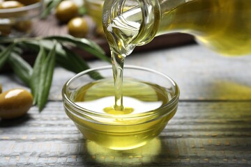 Pouring olive oil into bowl on wooden table, closeup. Healthy cooking