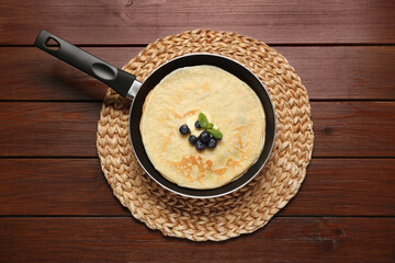 Delicious crepes with fresh berries, melting butter and mint on wooden table, top view