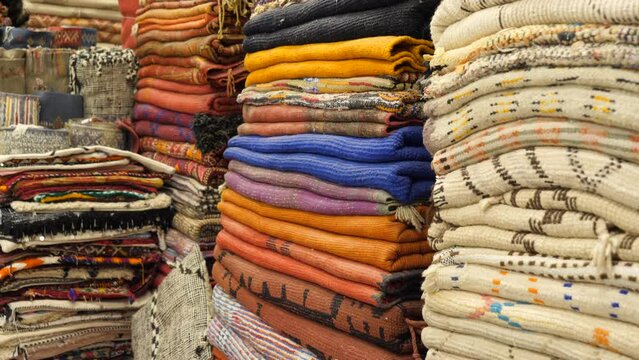 A set of handmade carpets and textiles stacked inside a Moroccan store.