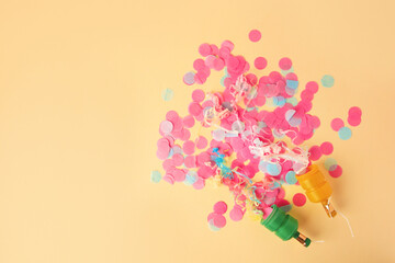 Colorful confetti and serpentine bursting out of party poppers on beige background, flat lay. Space for text