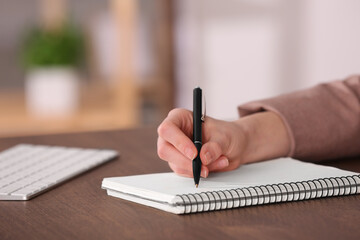 Fototapeta premium Woman writing in notebook at wooden table indoors, closeup. Space for text