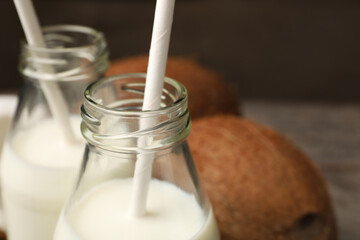 Glass bottles of delicious coconut milk on table, closeup. Space for text