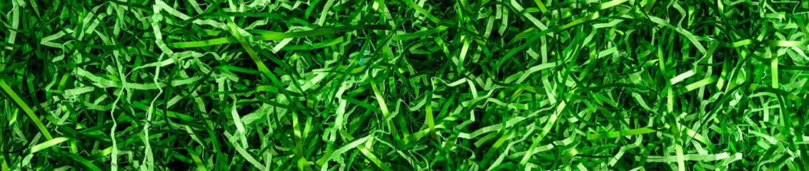 Easter grass, strips of green foil and lighter green paper, as a green background
