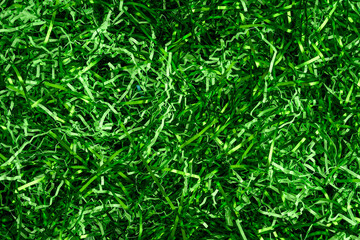 Easter grass, strips of green foil and lighter green paper, as a green background
