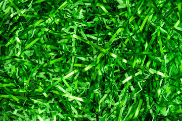 Easter grass, strips of green foil and lighter green paper, as a green background

