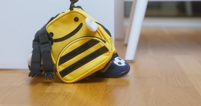 Yellow backpack accidentally falls on parquet and lies near white table. Yellow stripped backpack lies on floor waiting for owner to pick up closeup