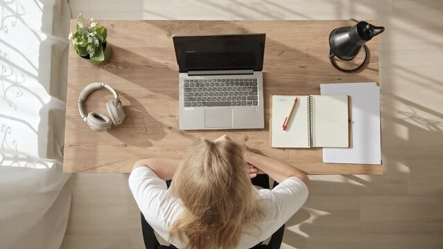 Top view, young blonde woman opens workbook while sitting at table and writes down first lesson. girl sits at home at her desk and computer, gets education.