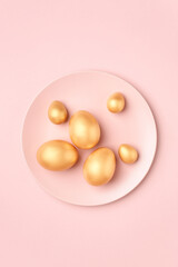 Golden Easter eggs on pastel pink plate. Luxury Easter greeting card in minimal style. Flat lay.