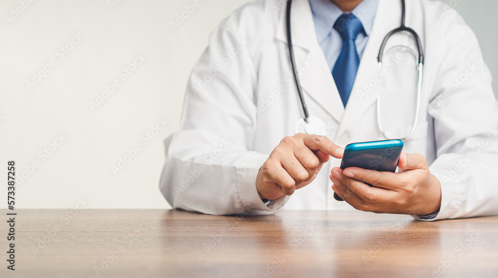 Poster doctor in a uniform with a stethoscope using a smartphone while sitting at the desk