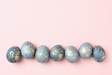 Blue and gold Easter eggs in row on pastel pink Easter background, greeting card, copy space, flat lay,