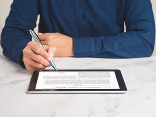 Businessman signing a digital contract or agreement on a tablet while sitting at the table in the office