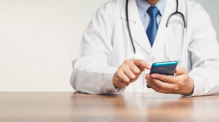 Doctor in a uniform with a stethoscope using a smartphone while sitting at the desk