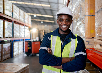 Professional Heavy Industry Engineer Worker Wearing Safety Uniform and Hard Hat. Smiling African American Industrial Specialist Walking in sparepart shelf in warehouse.