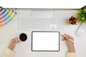 Minimal white workspace top view with a female graphic designer sipping coffee and using tablet