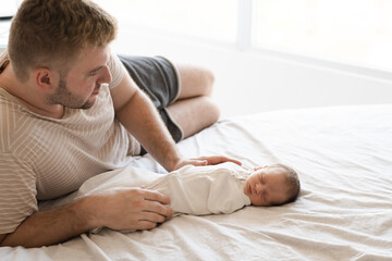 Happy man, father lying with child, caucasian hairy brunet cute newborn baby sleeping.One or two week child on bed indoor.Father's day and family concept.Copy space.