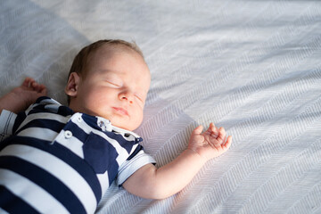 Little newborn caucasian brunet baby lying on back on bed wearing striped T-shirt sleeping.Half...