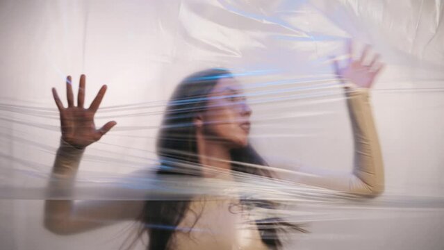 A Young Woman Is Trying To Break Through The Plastic. The Concept Of Pollution Of The Planet With Plastic.