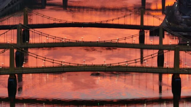 Roberto Clemente, Andy Warhol, and Rachel Carson bridges during orange sunset reflection on Allegheny river. Long aerial zoom and tilt up. Pittsburgh yellow bridges establishing shot.