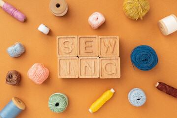 Fototapeta na wymiar Sewing tools: scissors, needles, thread, centimeter, paper pattern, flat layout. The word Sewing is laid out of wooden cubes. Bright sewing background, concept. Designer's workspace