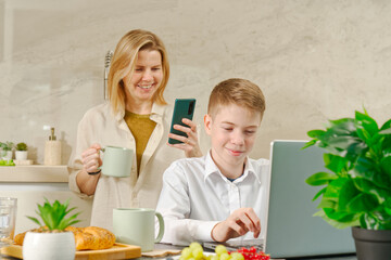 Happy mother and son have healthy breakfast in the kitchen at home. Happy mother and son in the kitchen. breakfast and digital devices Concept of happy family and healthy food.