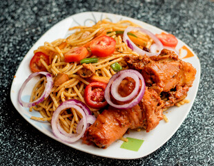 An assorted delicious dish of spaghetti noodles and chicken meat, garnished with sliced onions and tomatoes among other mouth watering food ingredients and spices cooked in Nigeria