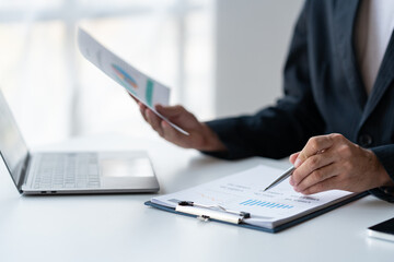 Obraz premium Young Asian businessman examining chart analyzing documents Financial data graph showing investment income in real estate business in office accounting management concept.