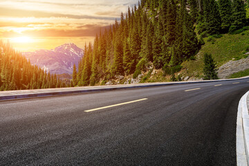 Asphalt road and green forest with mountain natural scenery at sunset in Xinjiang, China.