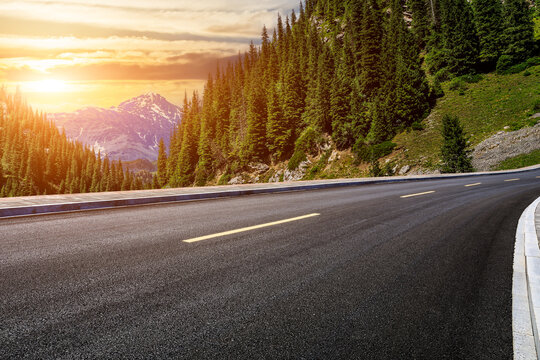Asphalt road and green forest with mountain natural scenery at sunset in Xinjiang, China.