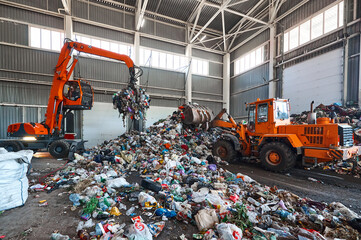 Grabbing excavator collects garbage in plant warehouse