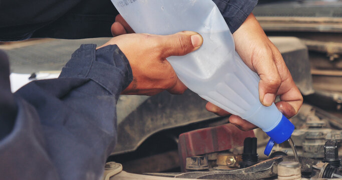 Car Mechanic man hands pouring Deionized purified Distilled water for car battery mechanical service. Close up hands man hold Deionized Distilled liquid water bottle at garage auto mobile car service