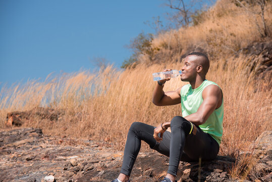 African American athletic man resting on the way sitting drinking water after running sport training outdoor in summer, workouts running and healthy lifestyle, sports and wellness.