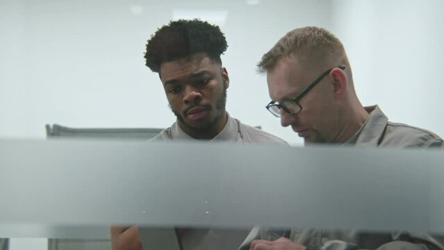 Two multi ethnic installers in uniform sets up security cameras or Internet in office room using laptop. They talk, check CCTV cameras in computer program. Concept of surveillance system and privacy.