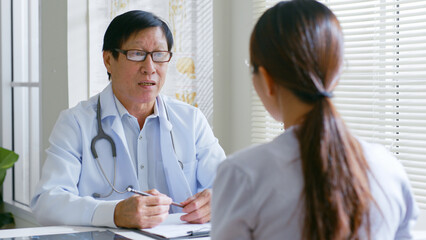 Senior Asian doctor describing the checking up result to a young woman patient in hospital, medical concept