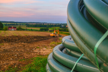 Water pipes and yellow excavator in the field. Carrying out water construction work.Plumbing installation.Bringing water to the house.