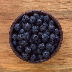 Fresh raw Patagonian Calafate berries (lat. Berberis heterophylla) in rustic bowl, photographed overhead on wood (Selective Focus, Focus on the berries)
