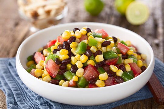 Mexican style colorful fresh vegetable salad made of beans, corn, tomato and bell pepper served in bowl, photographed on wood (Selective Focus, Focus in the middle of the image)