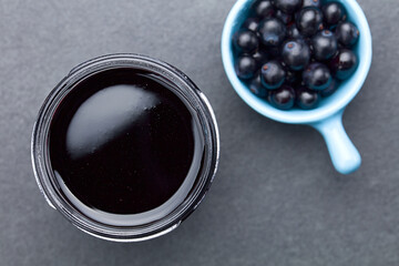 Fresh homemade jelly made of Patagonian Calafate berries (lat. Berberis heterophylla) in glass jar, photographed overhead on slate with a bowl of raw berries on the side (Selective Focus on the jelly)