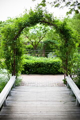 large garden trellis arch with greenery at the end of a wooden flat walkway bridge in a garden