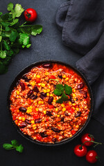 Chili con carne with beef, red beans, paprika, corn and hot peppers in tomato sauce, spicy tex-mex dish in a cooking pot, black table background, top view