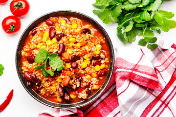 Chili con carne with beef, red beans, paprika, corn and hot peppers in tomato sauce, spicy tex-mex dish, white table background, top view