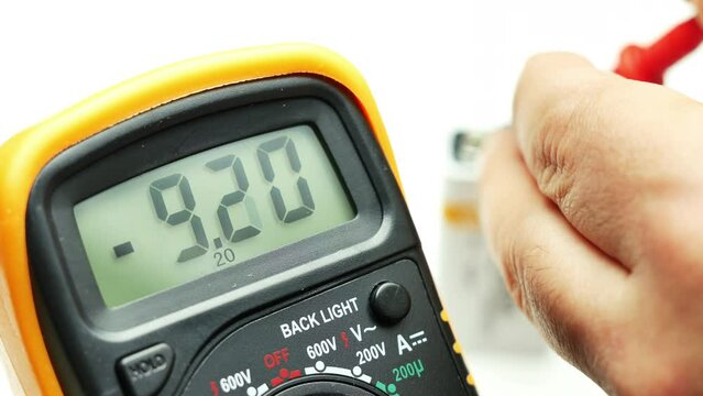 closeup hand using digital multimeter to measure level of charge of a battery